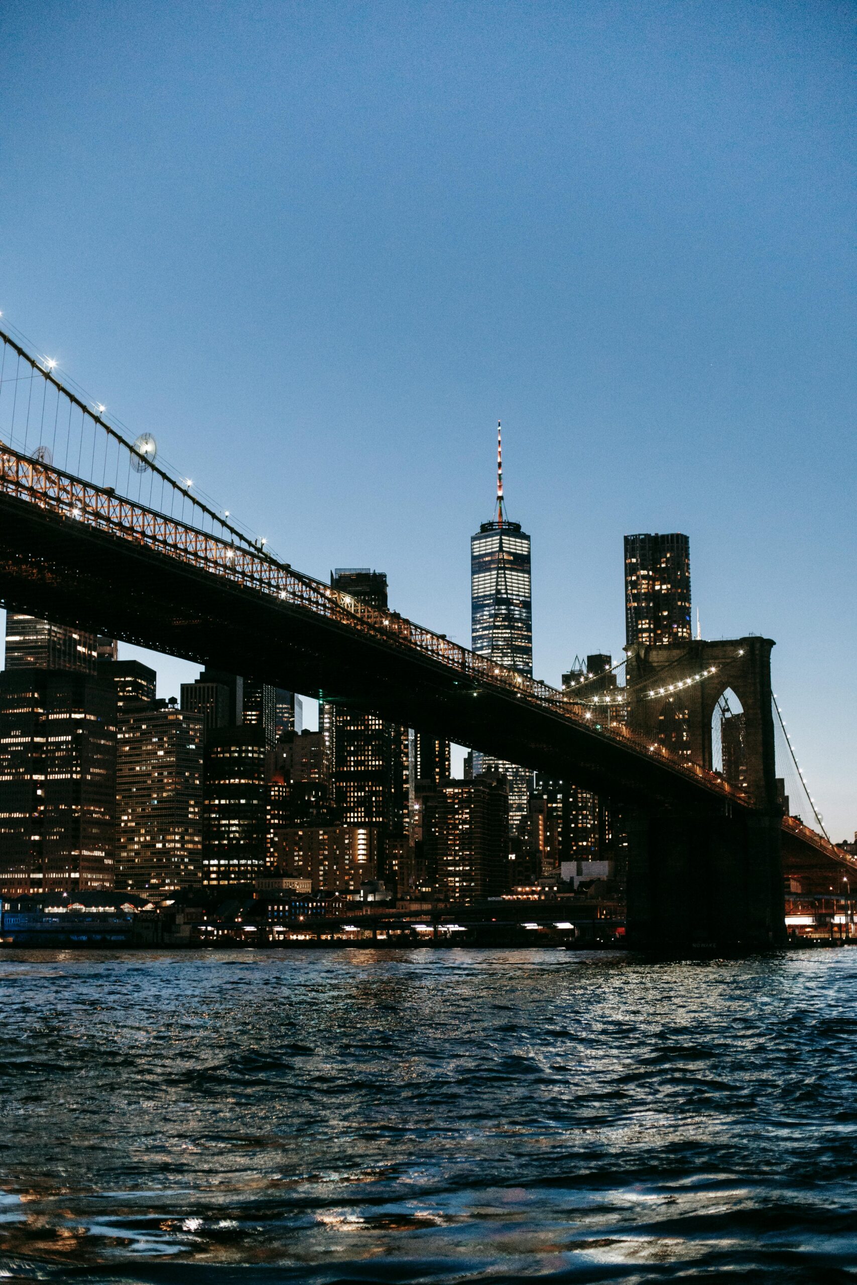 Captivating twilight view of Brooklyn Bridge and illuminated New York City skyline over the river.